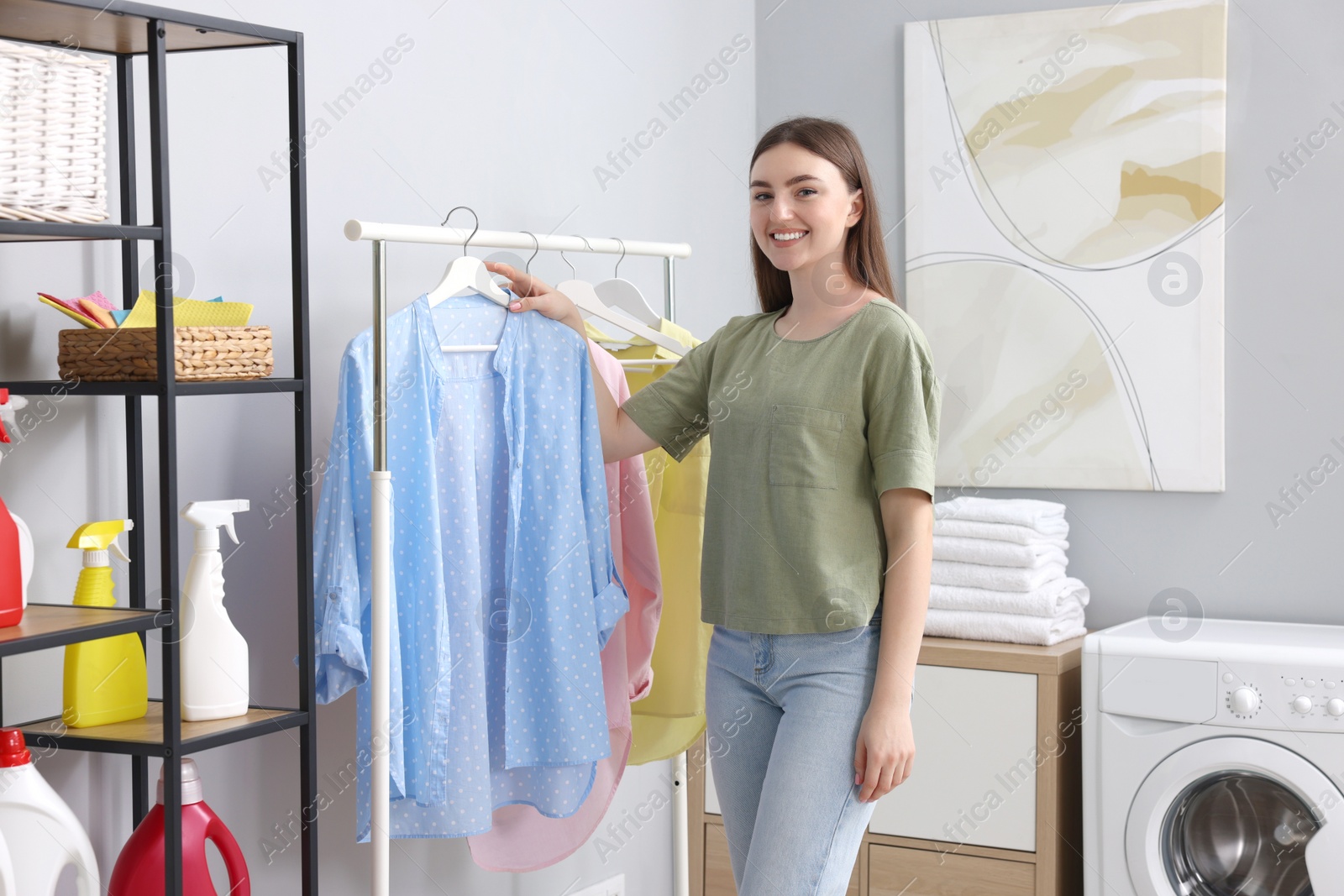 Photo of Young woman taking shirt from rack in laundry room