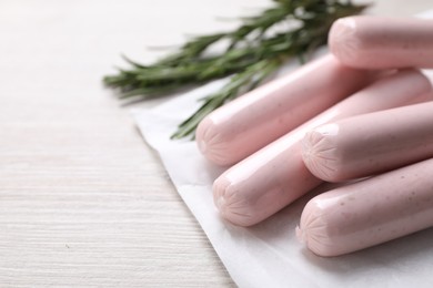 Photo of Vegan sausages and rosemary on white wooden table, closeup. Space for text