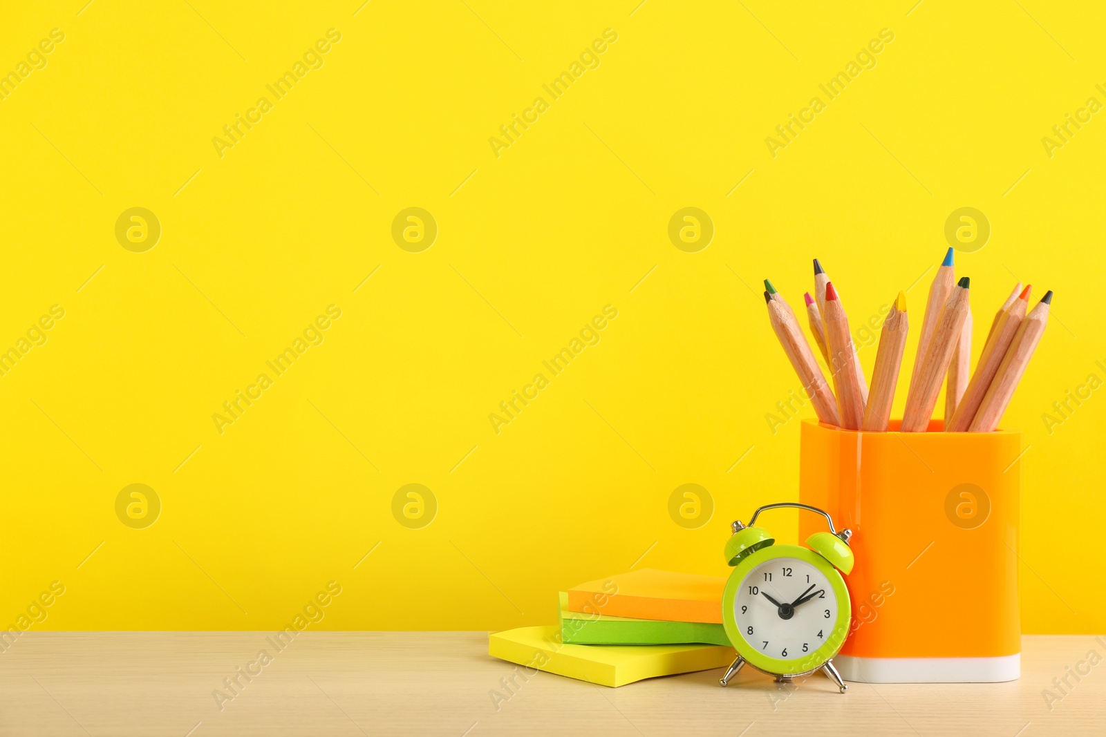 Photo of Different school stationery and alarm clock on table against yellow background, space for text. Back to school