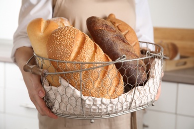 Baker holding basket of fresh bread indoors, closeup