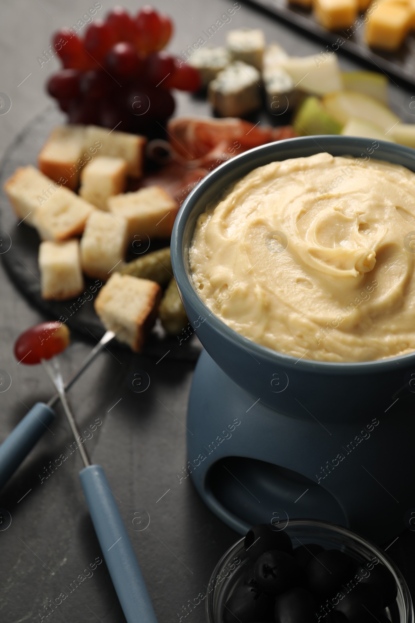 Photo of Fondue with tasty melted cheese, forks and different snacks on black table