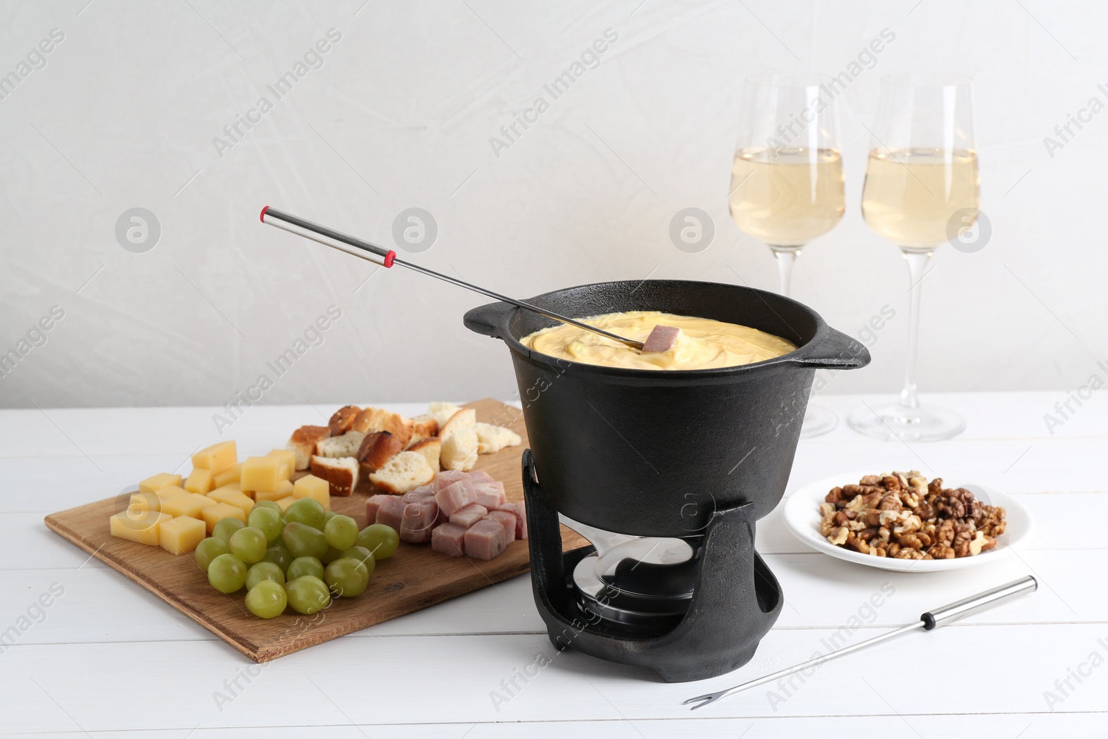 Photo of Fondue pot with tasty melted cheese, forks, wine and different snacks on white wooden table