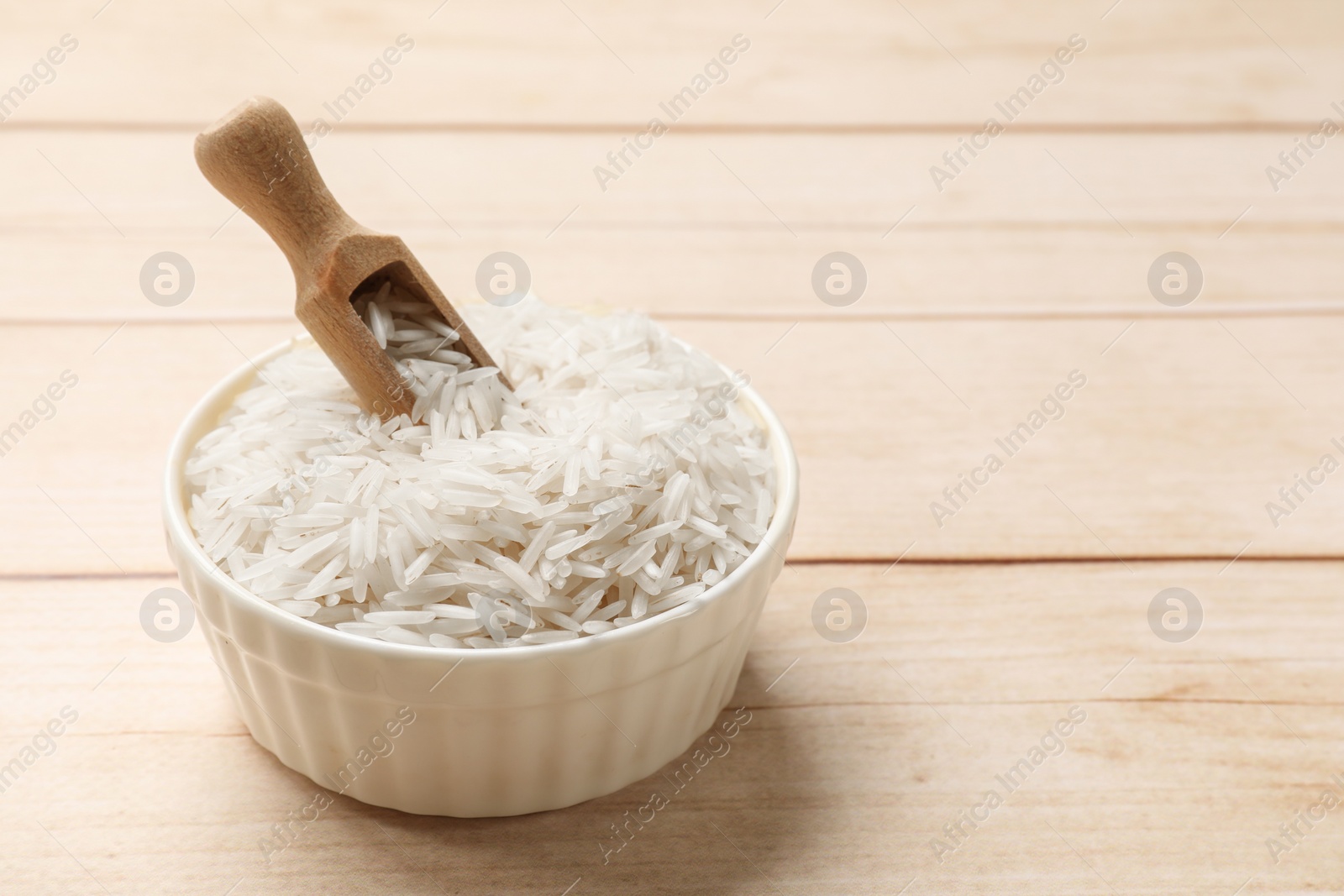 Photo of Raw basmati rice and scoop in bowl on white wooden table, space for text