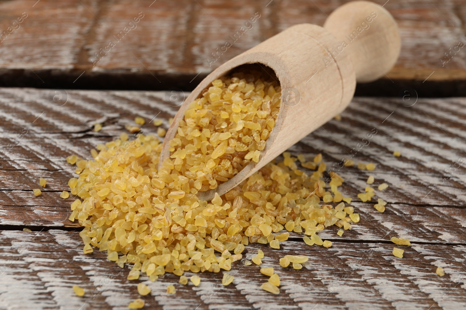 Photo of Scoop with raw bulgur on wooden table, closeup
