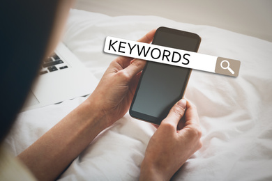 Woman with smartphone searching for keywords on bed, closeup