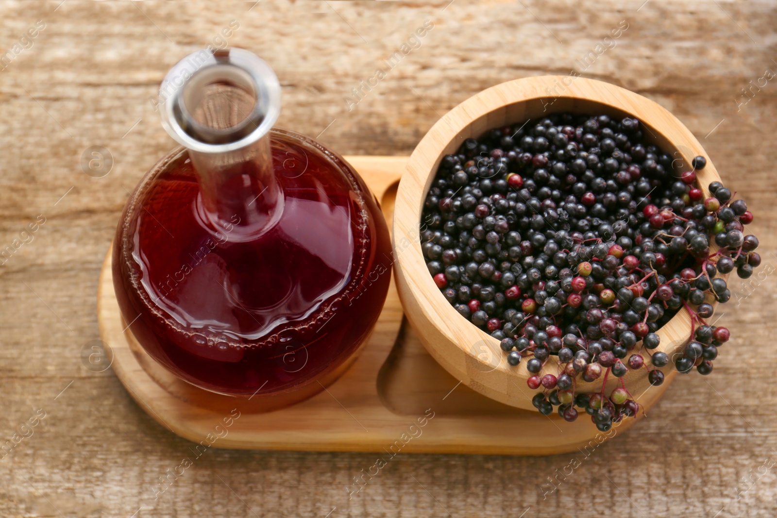 Photo of Elderberry wine and bowl with Sambucus berries on wooden table, above view