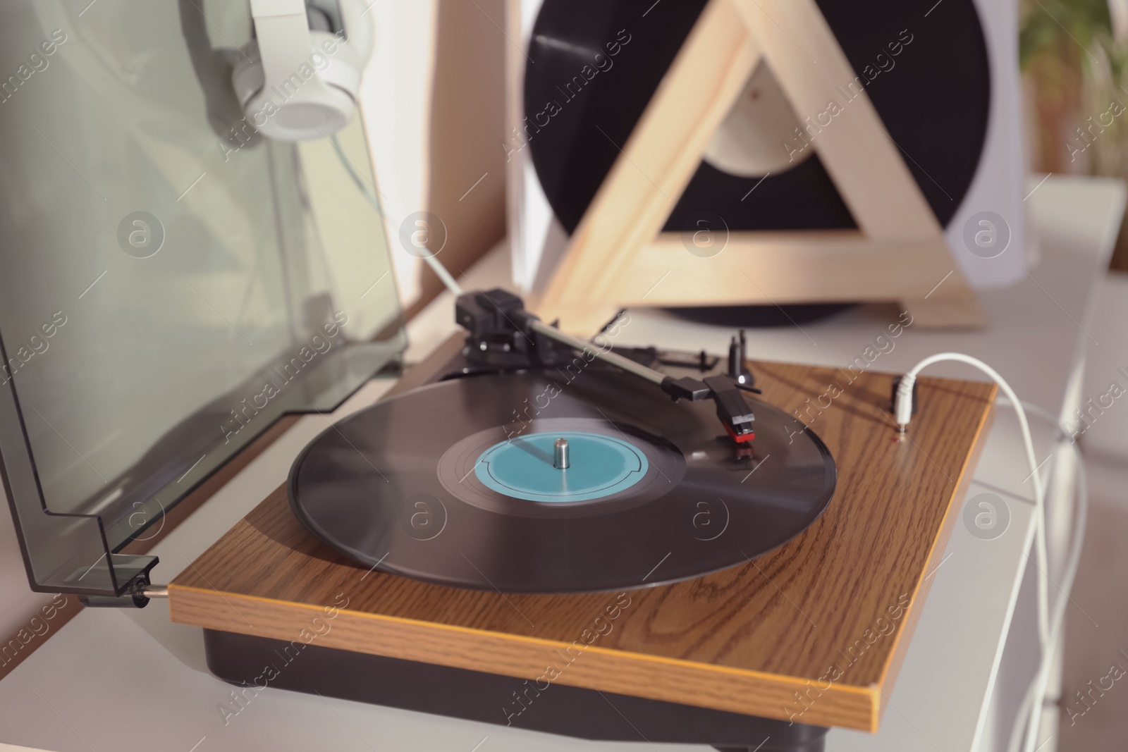 Photo of Stylish turntable with vinyl disc and headphones on white chest of drawers at home