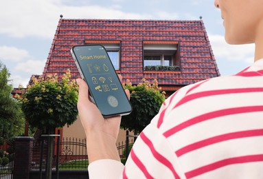 Image of Woman using smart home control system via mobile phone near house outdoors, closeup