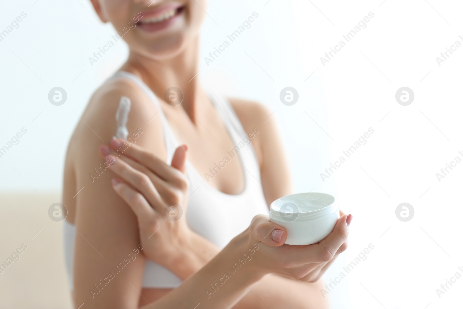 Photo of Young woman with jar of body cream at home