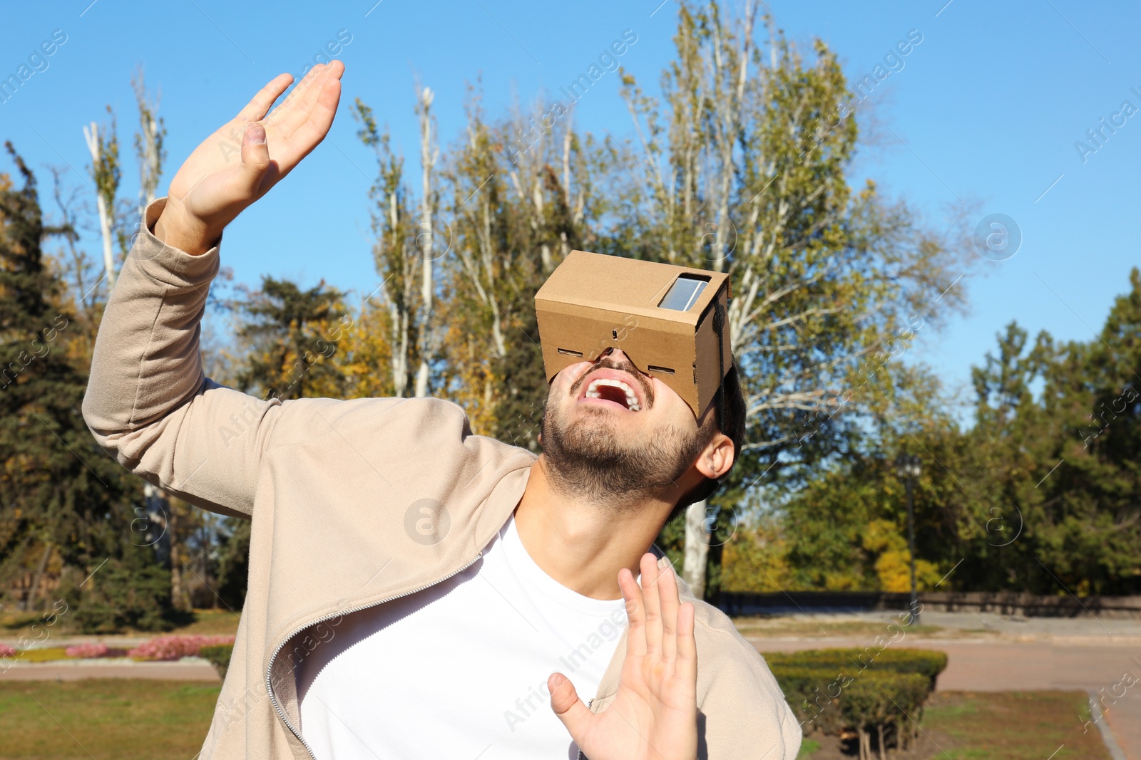 Photo of Young man using cardboard virtual reality headset outdoors