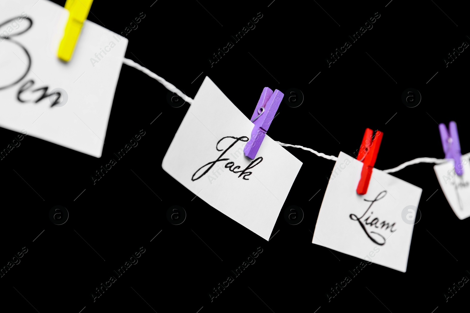 Photo of Paper pieces with baby names on rope against black background, closeup