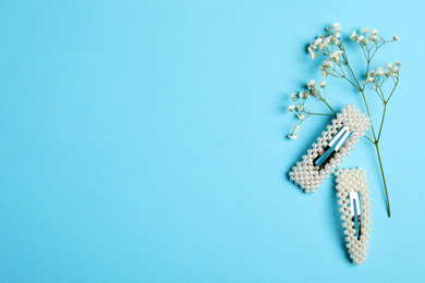 Stylish hair clips and flowers on light blue background, flat lay. Space for text