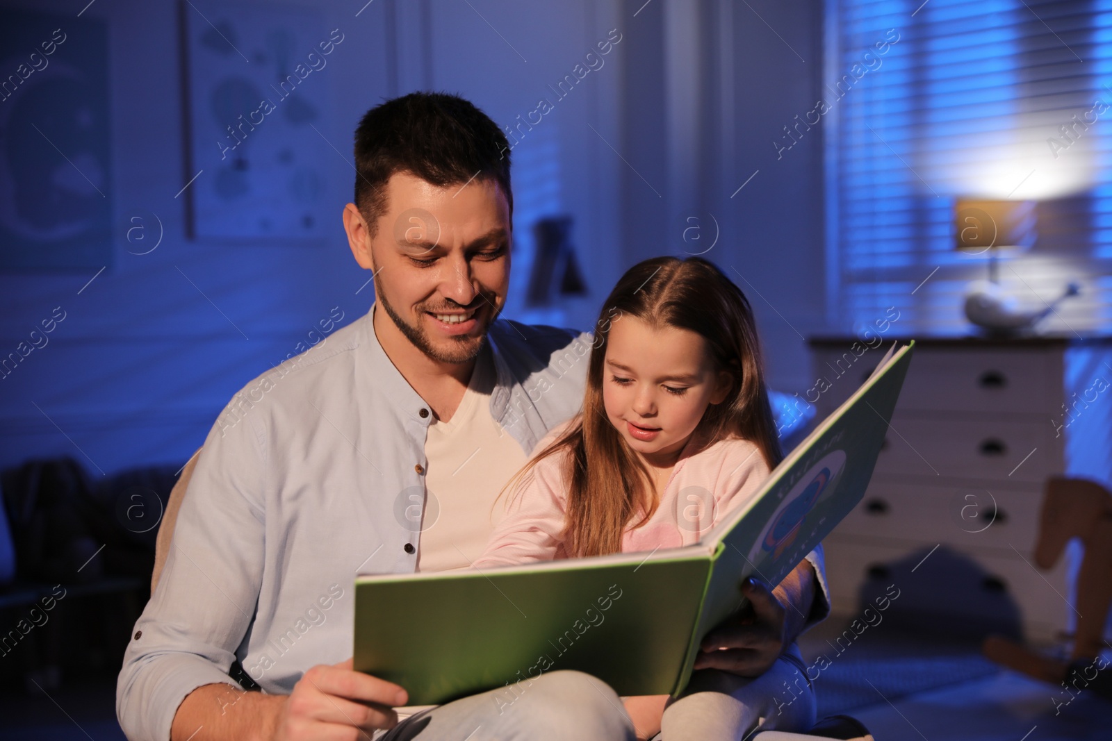 Photo of Father reading bedtime story to his daughter at home