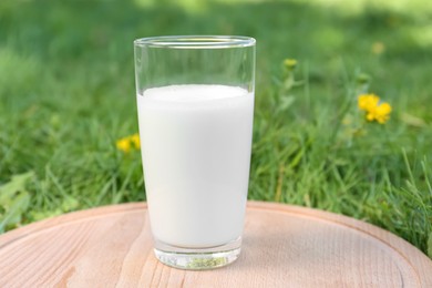 Photo of Glass of fresh milk on wooden board outdoors