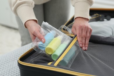 Photo of Woman with plastic bag of cosmetic travel kit packing suitcase at home, closeup. Bath accessories