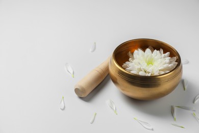 Photo of Tibetan singing bowl with water, beautiful chrysanthemum flower and mallet on white background, space for text
