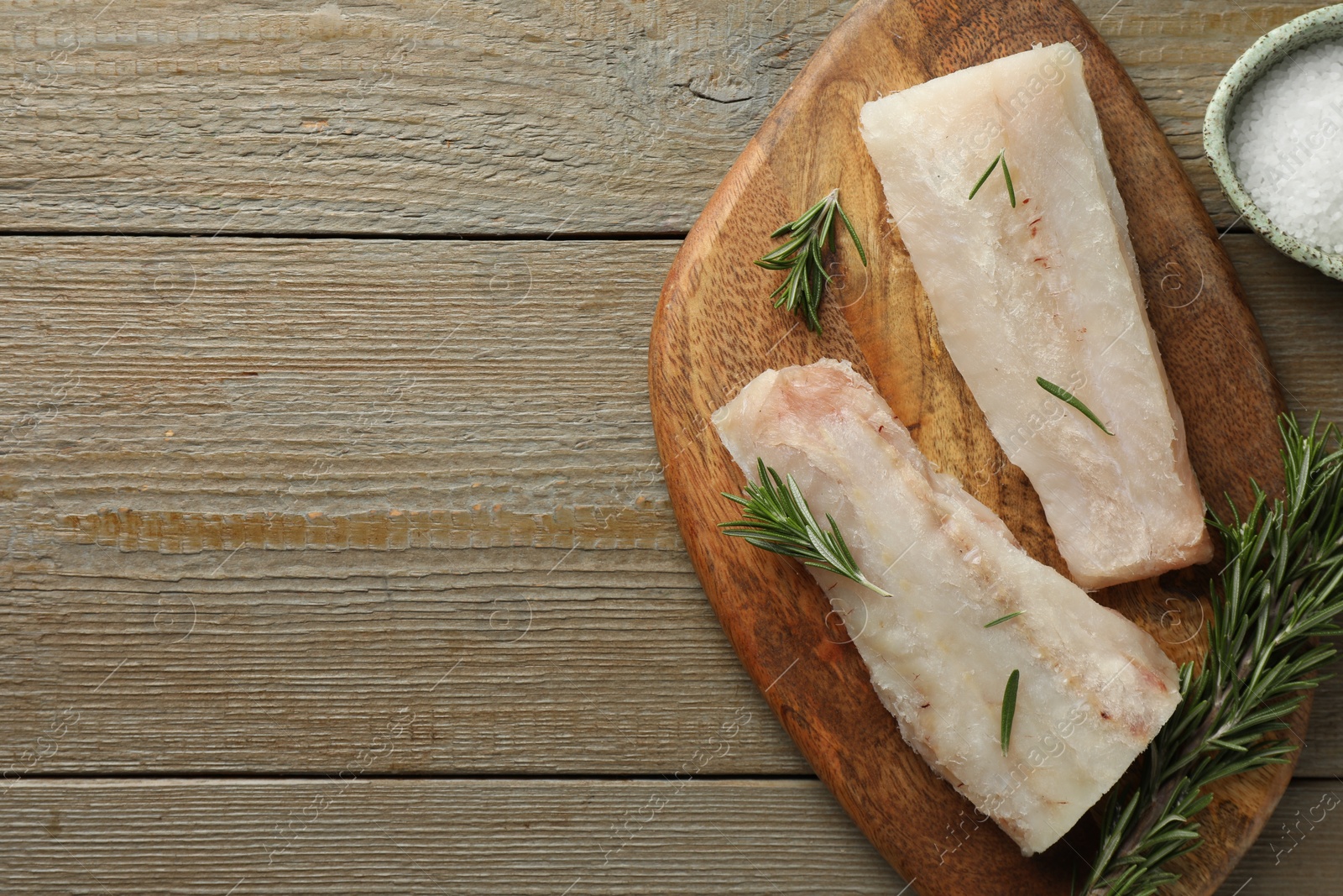 Photo of Fresh raw cod fillets, salt and rosemary on wooden table, flat lay. Space for text