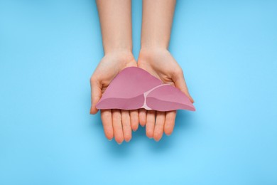 Photo of Woman holding paper liver on light blue background, closeup and top view. Hepatitis treatment