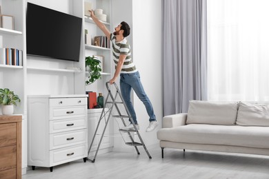 Man on metal folding ladder taking books from shelf at home