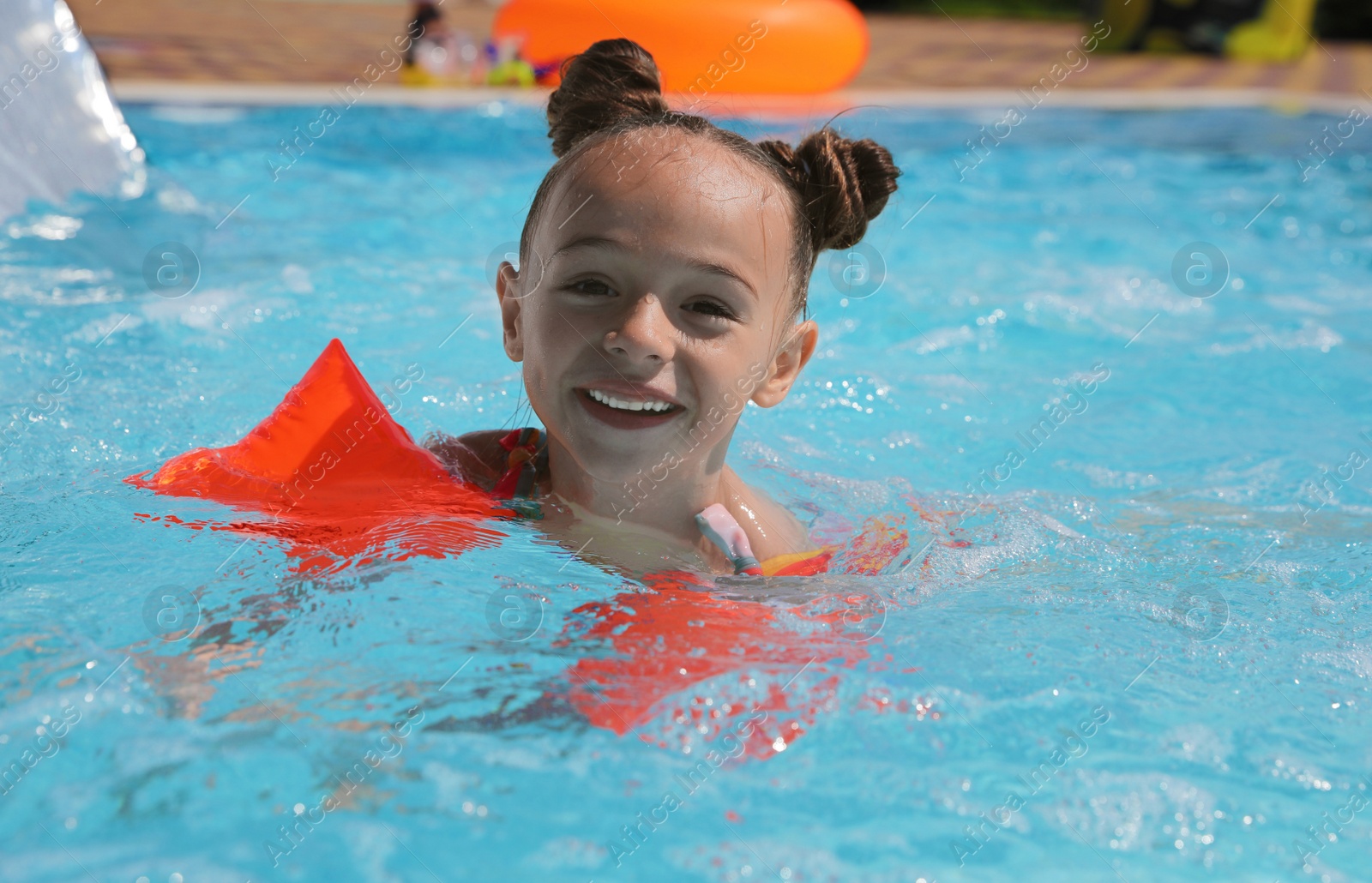 Photo of Cute little girl with inflatable sleeves in swimming pool at water park