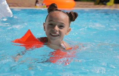 Cute little girl with inflatable sleeves in swimming pool at water park