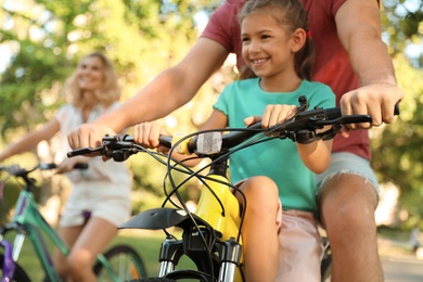 Happy family with daughter riding bicycles in park
