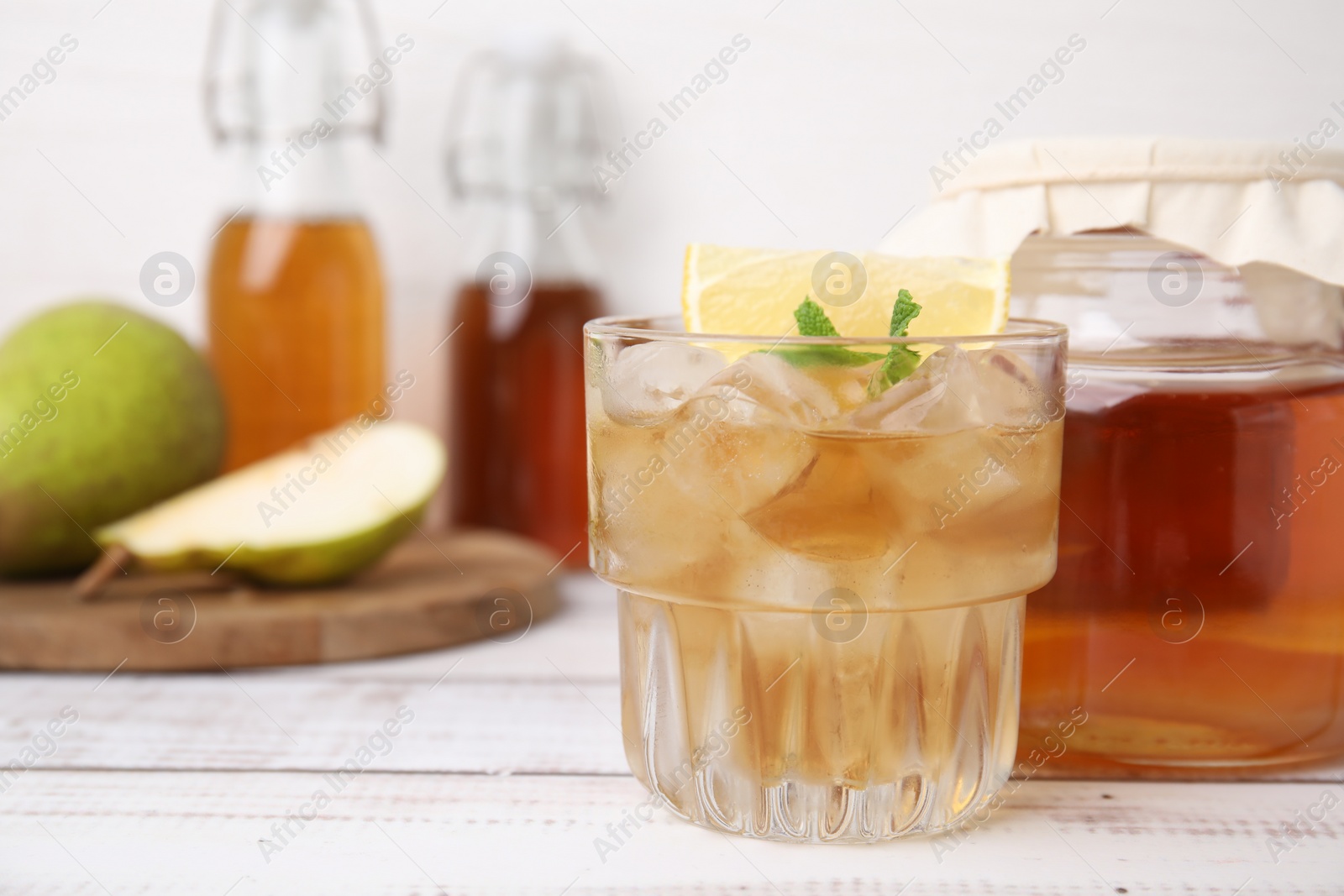 Photo of Tasty kombucha and ice cubes in glass on white wooden table, closeup. Space for text