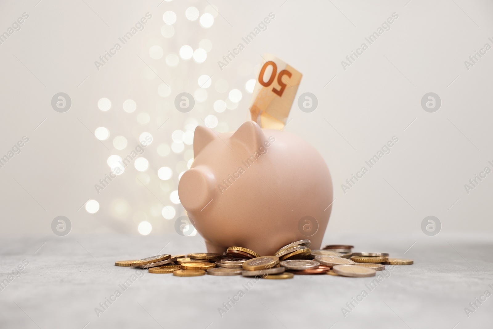 Photo of Piggy bank and coins on grey table against blurred lights