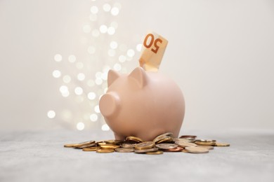 Photo of Piggy bank and coins on grey table against blurred lights