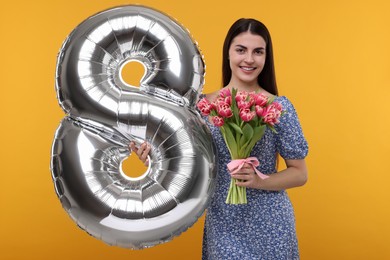 Happy Women's Day. Charming lady holding bouquet of beautiful flowers and balloon in shape of number 8 on orange background