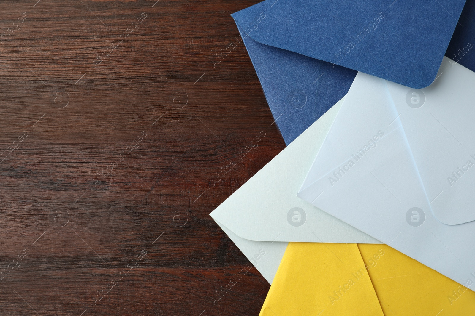 Photo of Colorful paper envelopes on wooden table, top view. Space for text