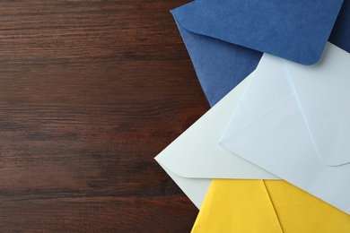 Colorful paper envelopes on wooden table, top view. Space for text