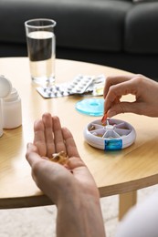 Woman with pills, organizer and glass of water at light wooden table, closeup