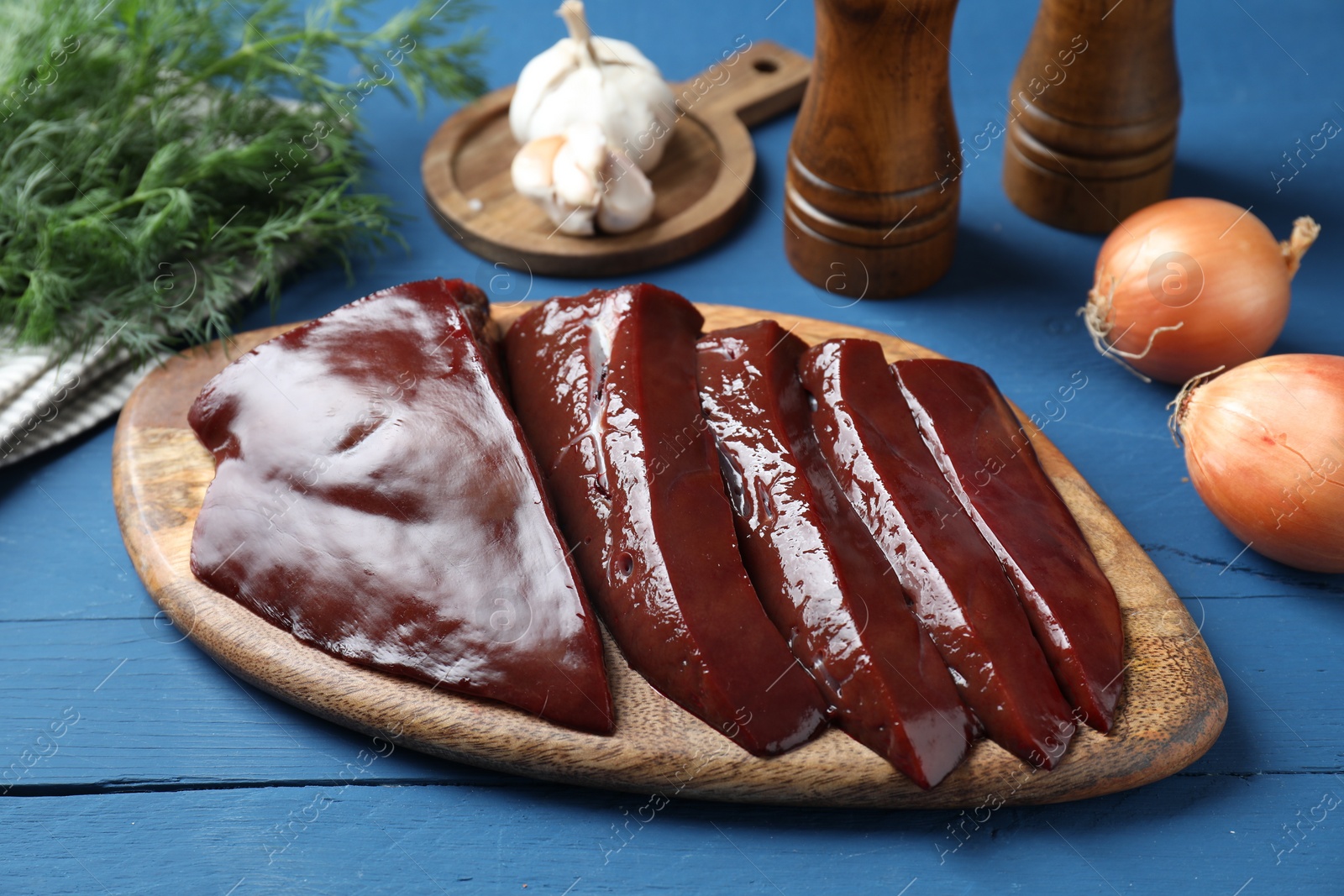 Photo of Cut raw beef liver with onions, garlic, dill and spices on blue wooden table, closeup