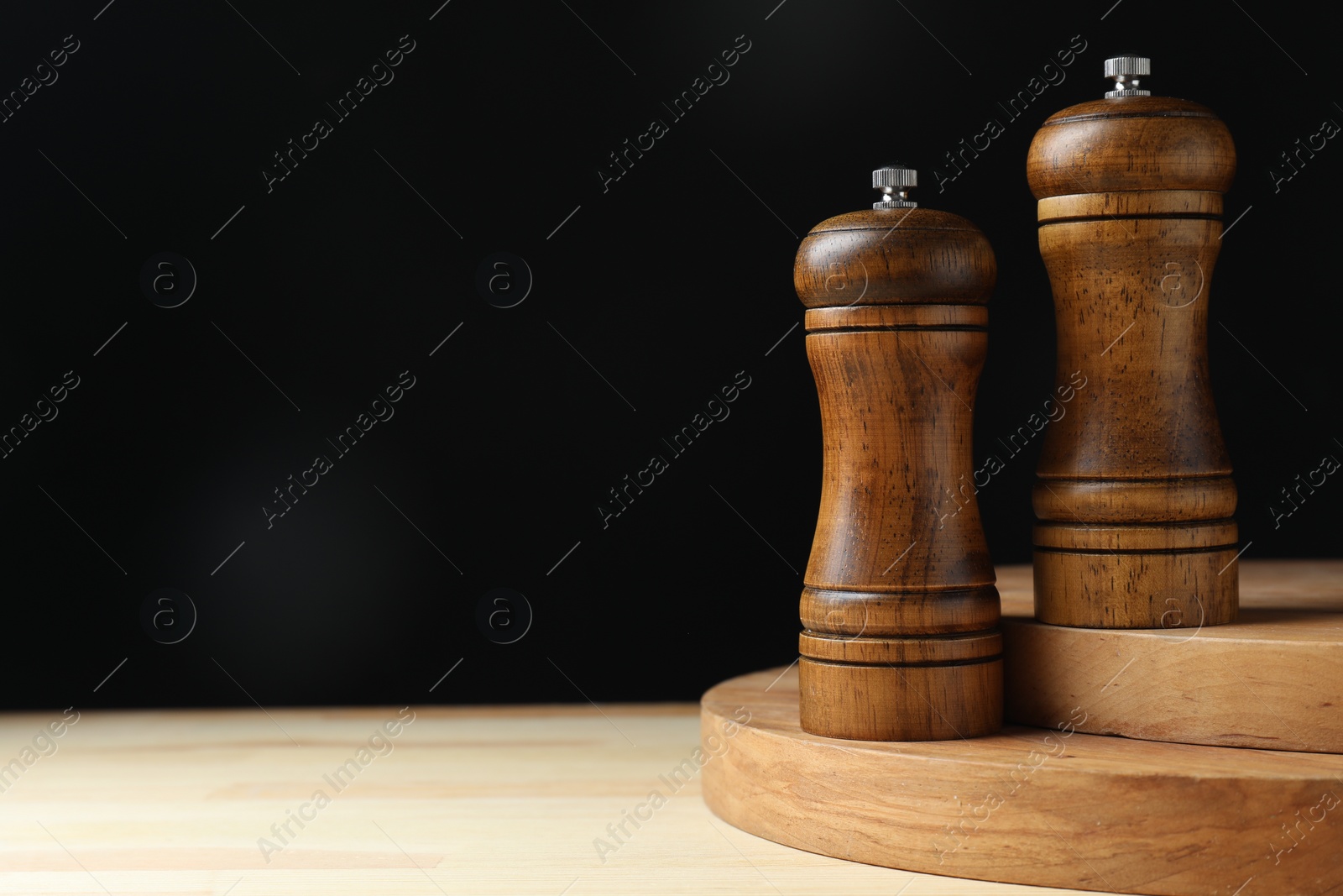 Photo of Salt and pepper shakers on wooden table against black background, space for text