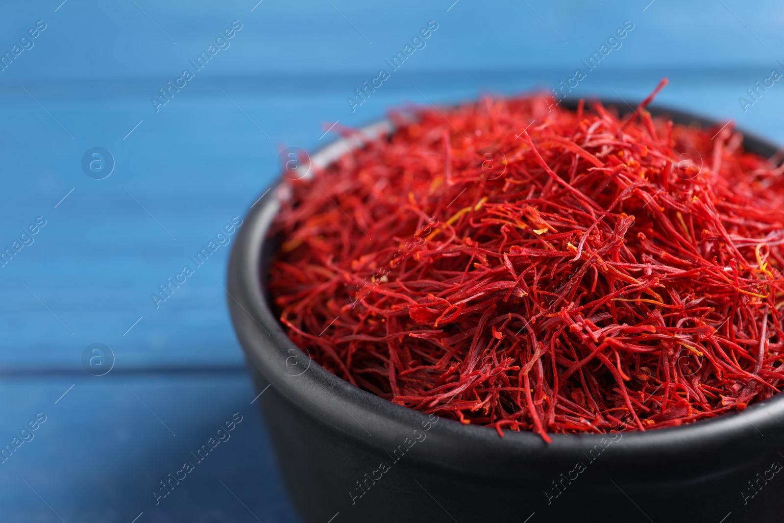 Photo of Dried saffron in bowl on blue table, closeup