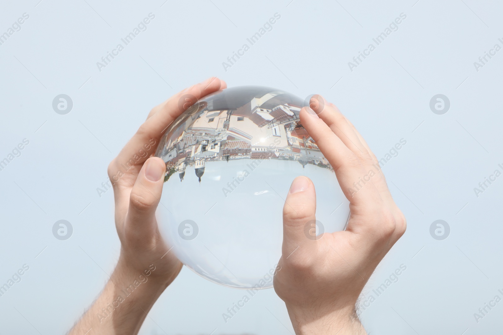 Photo of View of beautiful city street, overturned reflection. Man holding crystal ball against sky, closeup