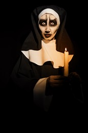 Photo of Scary devilish nun with burning candle on black background. Halloween party look