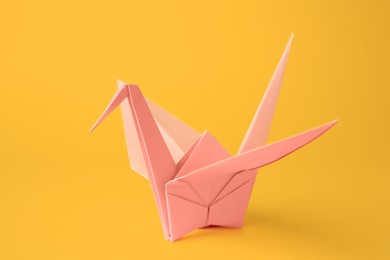 Origami art. Beautiful pale pink paper crane on orange background