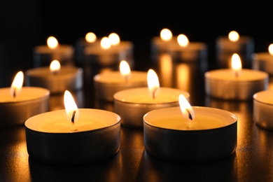 Photo of Wax candles burning on table in darkness, closeup