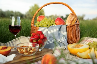 Picnic blanket with delicious food and wine on green grass