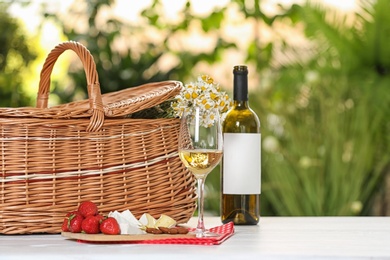 Photo of Picnic basket and wine with products on table against blurred background, space for text