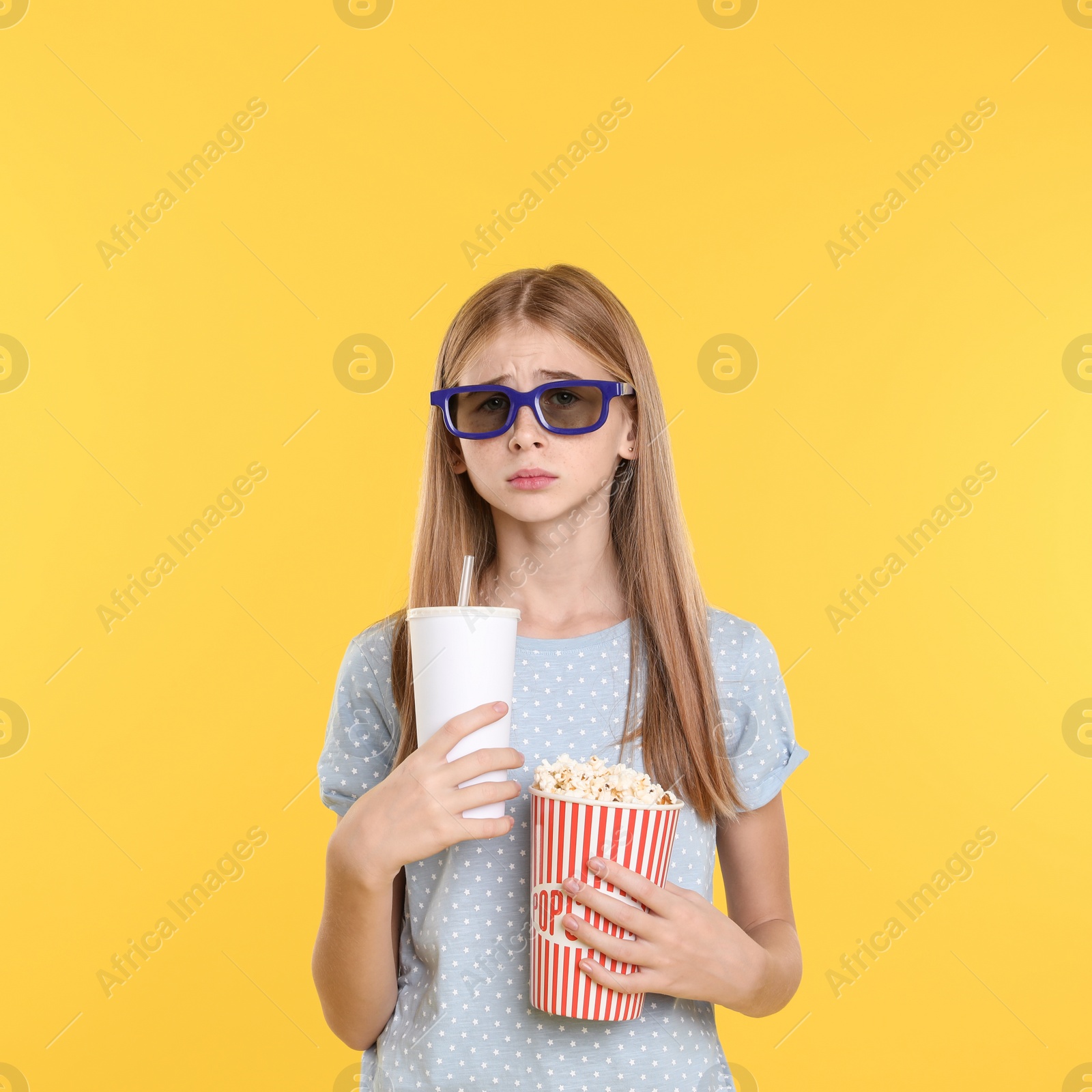Photo of Emotional teenage girl with 3D glasses, popcorn and beverage during cinema show on color background
