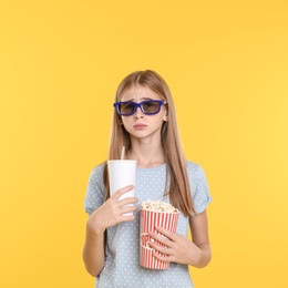 Emotional teenage girl with 3D glasses, popcorn and beverage during cinema show on color background