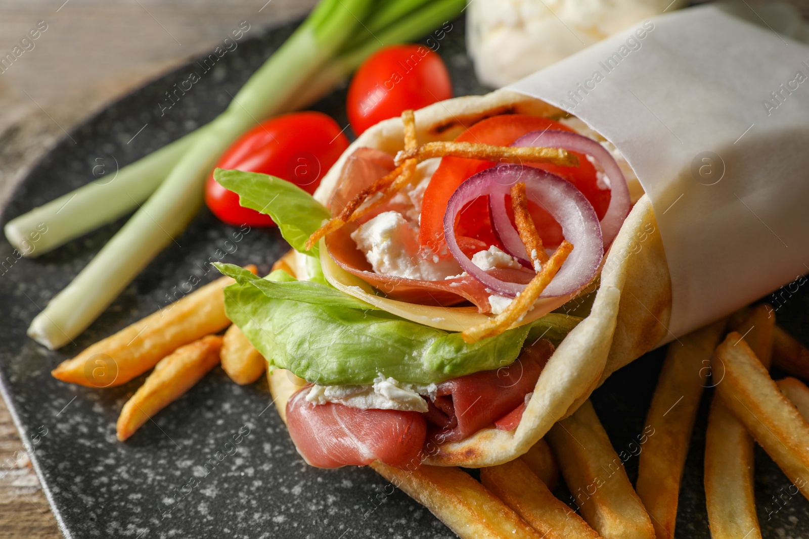Photo of Delicious pita wrap with prosciutto, vegetables and potato fries on wooden table, closeup