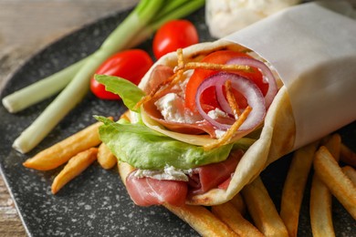 Photo of Delicious pita wrap with prosciutto, vegetables and potato fries on wooden table, closeup