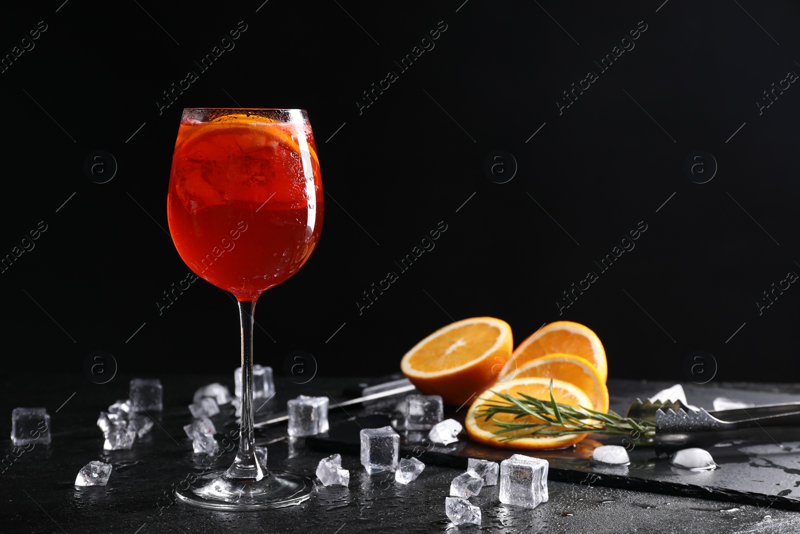 Photo of Glass of tasty Aperol spritz cocktail with orange slices and ice cubes on table against black background, space for text