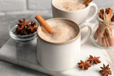 Cups of delicious eggnog with anise and cinnamon on light grey table