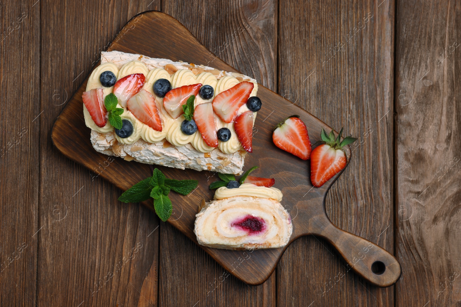 Photo of Tasty meringue roll with jam, cream, strawberry, blueberry and mint on wooden table, top view