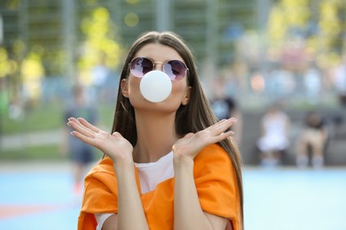 Photo of Beautiful young woman in sunglasses blowing bubble gum outdoors